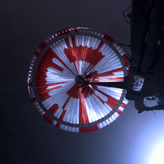 The Perseverance parachute photographed from below during descent, its red and white gores encoding a message in binary